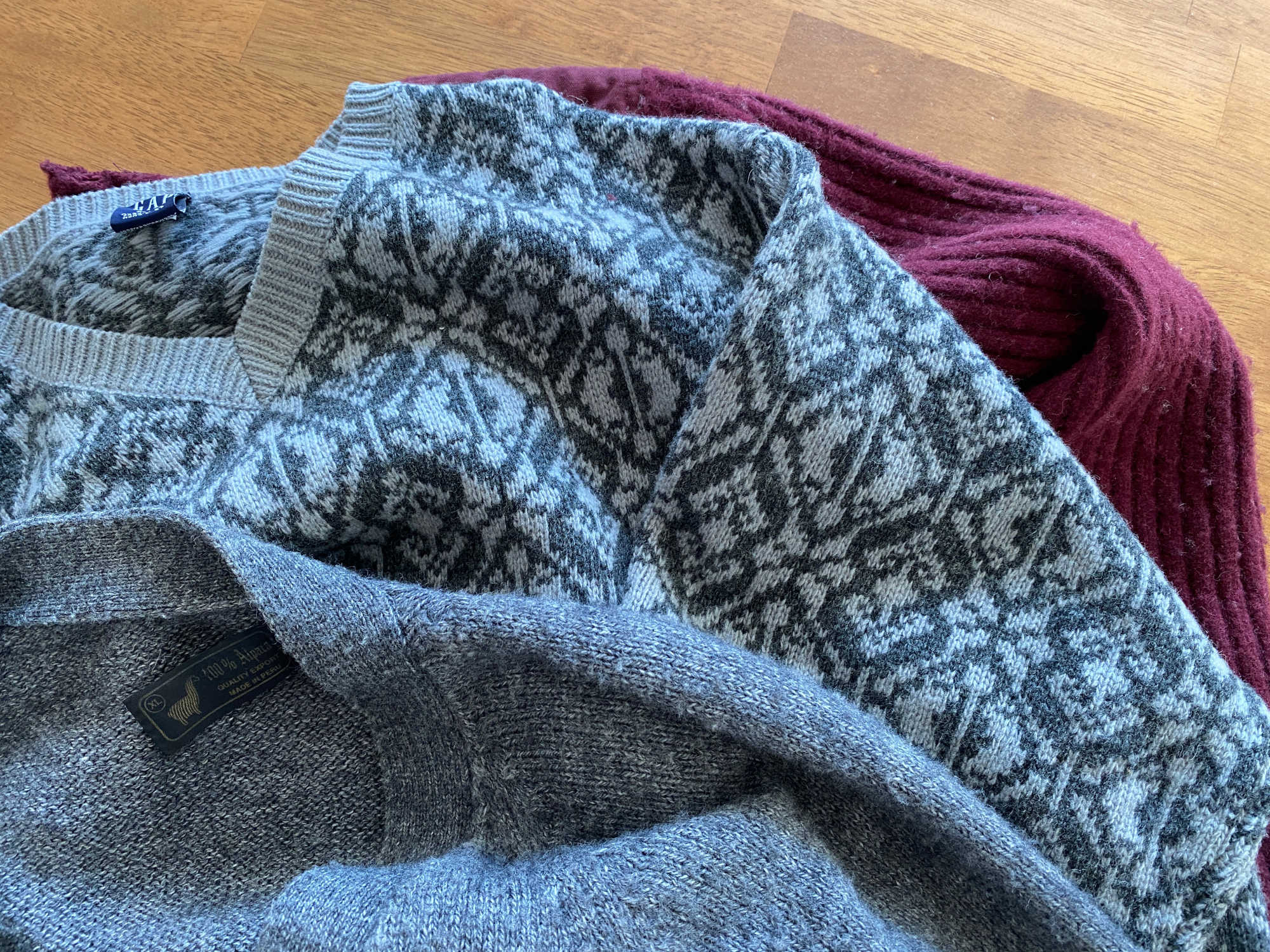 Two wool sweaters (one grey, one maroon), lying on a wooden table. The sweaters have been thrifted from a local Deseret Industries.